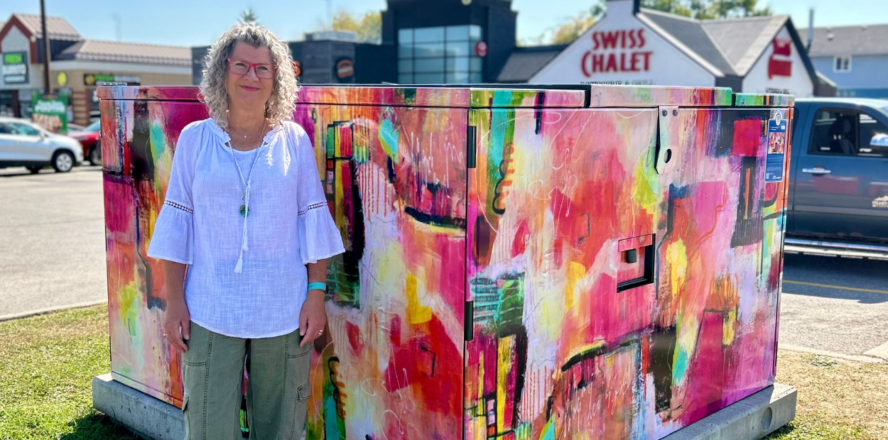 A woman stands in front of a large hydro box that is wrapped in abstract art.